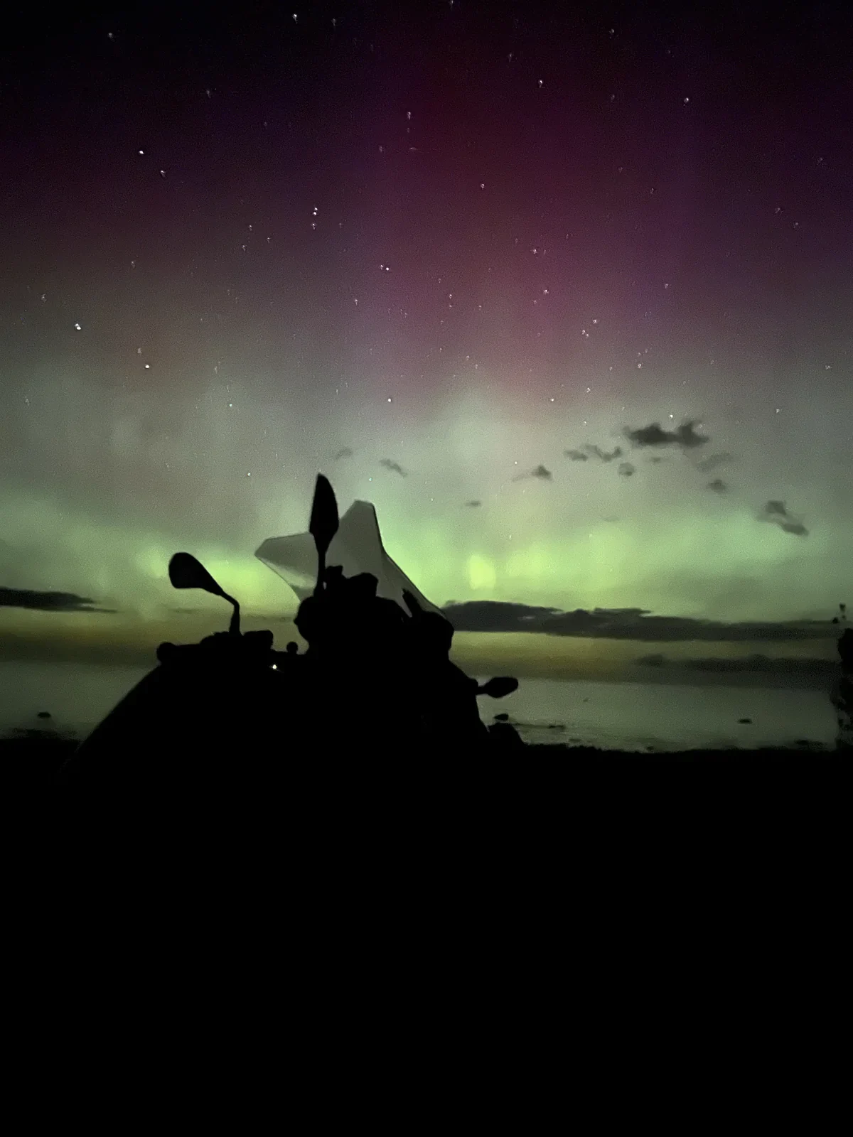 Adventure motorcycle silhouetted beneath the northern lights during Paul Larson’s multi-month journey.