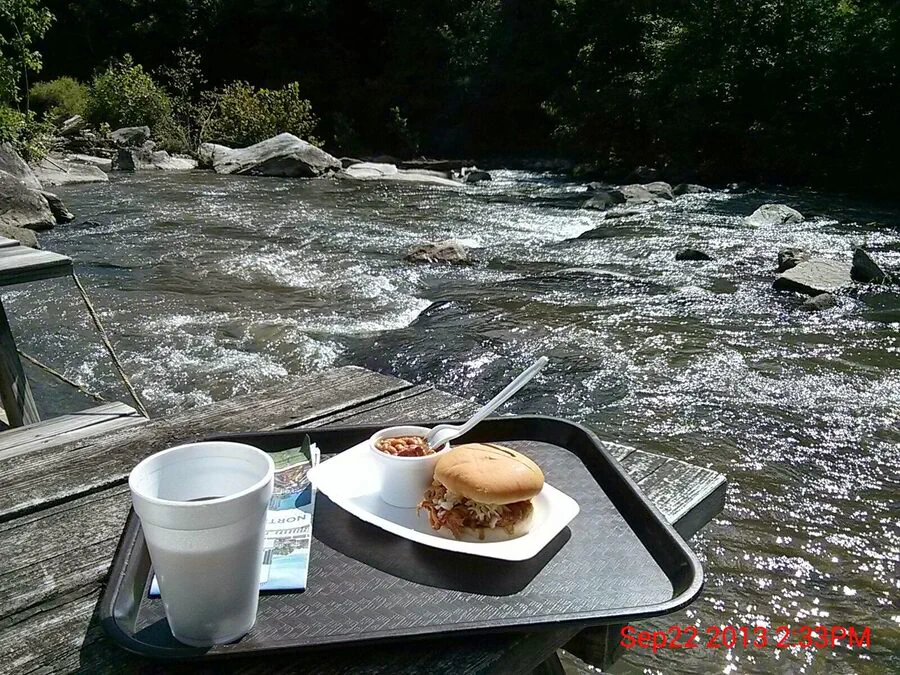 Barbecue sandwich and beans on an outdoor table beside the river.