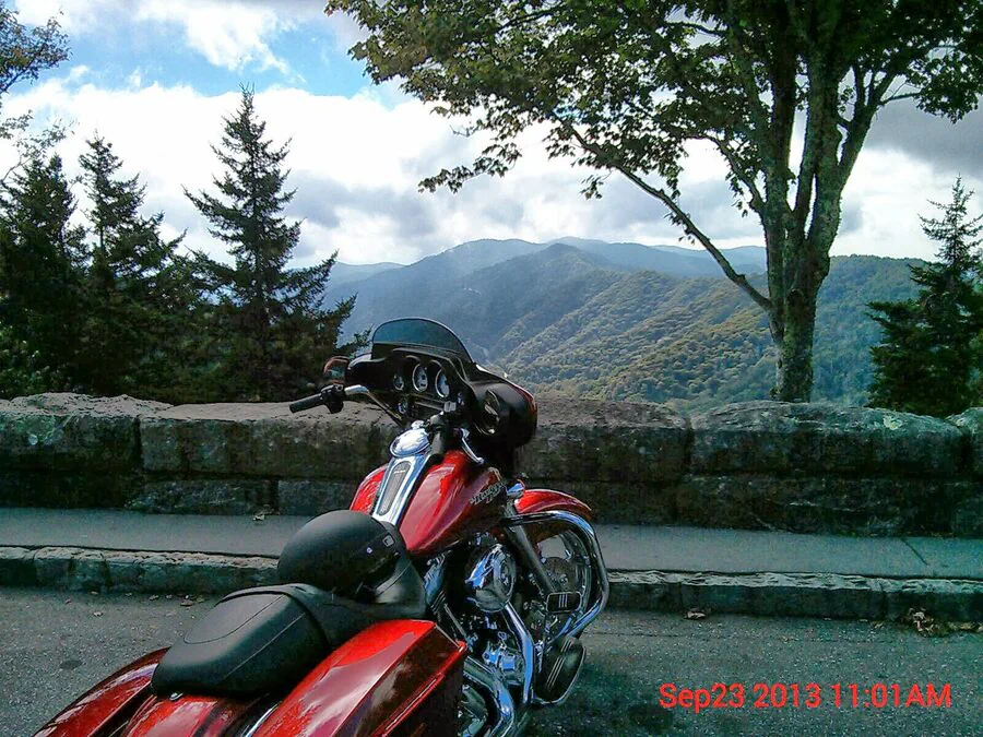 Red touring motorcycle at an overlook with mountain ridges stretching into the distance.