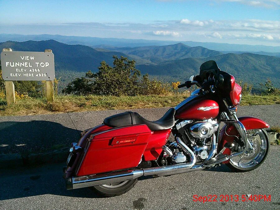 Red touring motorcycle beside the Funnel Top elevation sign with mountain ridges in the distance.