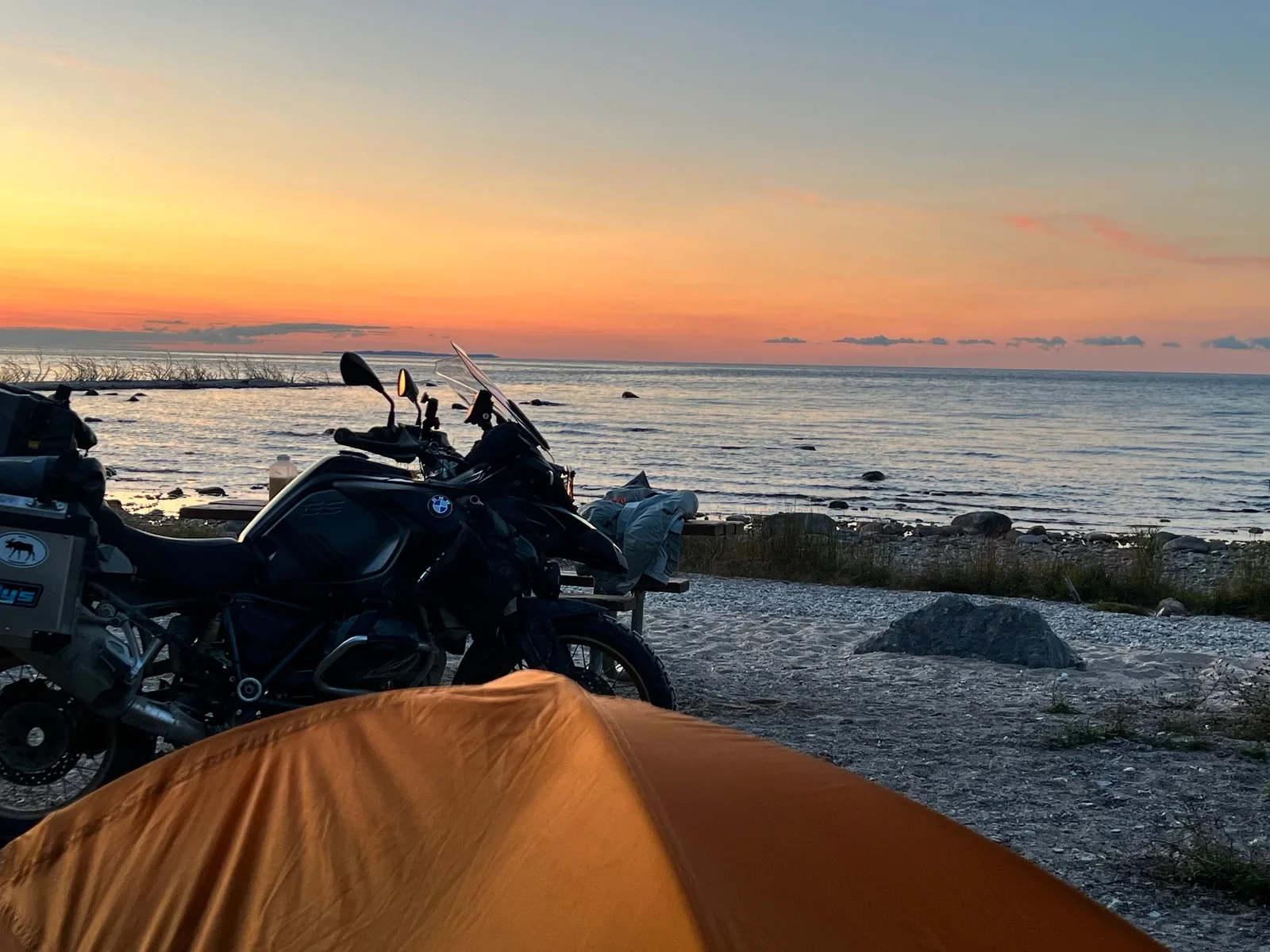 Tent and BMW adventure motorcycle beside the water at sunset during Paul Larson’s long-distance journey.